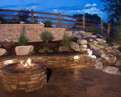 "Round stone fire pit and interlocking paver patio with a built-in retaining wall bench in a Sugar Hill, Georgia garden by Nature's Canvas."